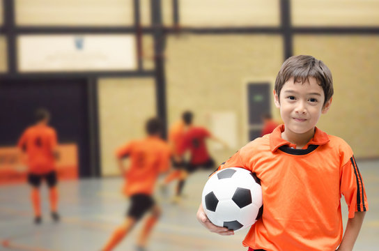 Little boy holding football in futsal gym