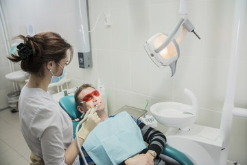 Fototapeta na wymiar dental care concept stomatology inspection. the patient lies in a chair in dentistry in front of him a hand with drill. the dentist is in the office beside the chair with the patient