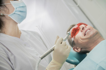 dental care concept stomatology inspection. the patient lies in a chair in dentistry in front of him a hand with drill. the dentist is in the office beside the chair with the patient