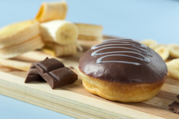 Delicious donut with banana and chocolate. Served on the wooden board. Decorated with banana. Blue background. Horizontal image.