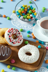 Delicious donuts with chocolate, coconut and strawberry. Served on the wooden board and white napkin. Decorated with multicolored candy and cup of coffee. Blue background. Vertical image.