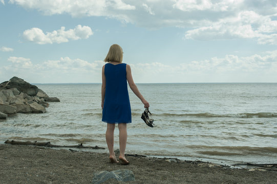 девушка босяком стоит на берегу моря и смотрит вдаль . barefoot girl standing on the beach and looks into the distance
