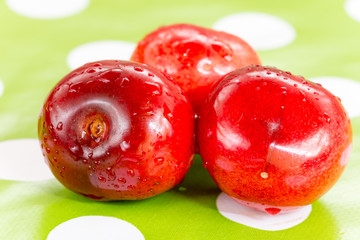 Three cherries on the table cloth with blurred background