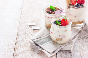 Homemade italian dessert tiramisu with strawberries, mint and cocoa in glass jars, closeup.