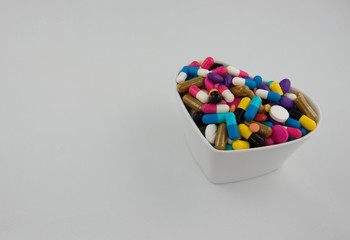 Colorful pills and capsule in a cup on white background