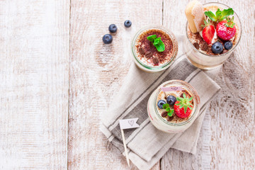 Homemade italian dessert tiramisu with strawberries, mint and cocoa in glass jars, top view