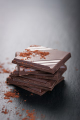Stack of chocolate chunks on a dark stone background with cocoa, closeup