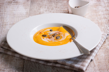 Homemade tasty creamy pumpkin soup puree in a bowl on a wooden background.