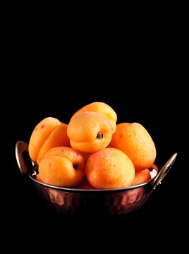 Organic apricots in a copper plate on a black background.