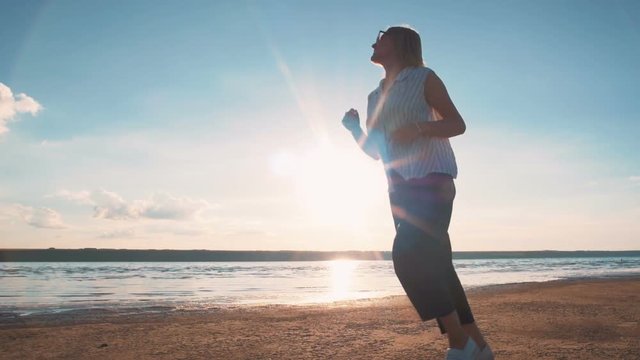Young attractive woman running and having a lot of fun on the beach during sunset or sunrise, slow motion