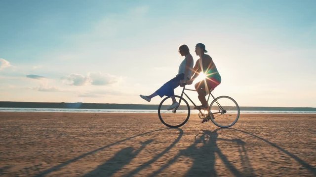 Young woman and man riding a bicycle at the shore and having some fun, slow motion