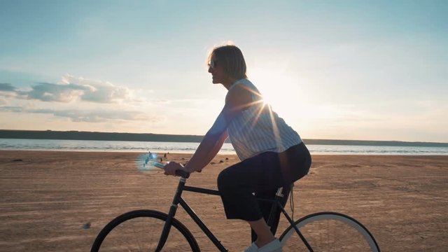 Young attractive woman riding vintage bike on the beach near the sea during sunset ot sunrise, slow motion