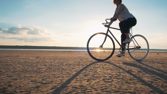Young attractive woman riding vintage bike on the beach near the sea during sunset ot sunrise, slow motion