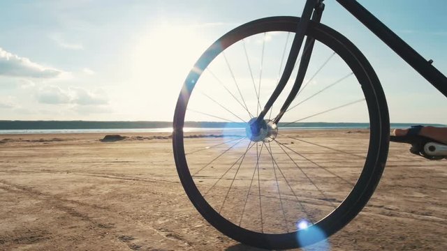 Close up shot of man riding vintage bike at the beach during sunset or sunrise, slow motion