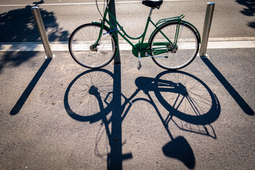 Fototapeta na wymiar Bicicletta da donna parcheggiata e legata a un palo e la sua ombra