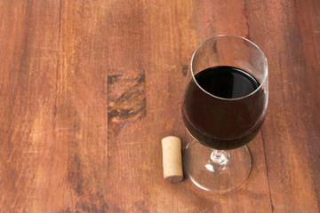 Glass of red wine and cork on wooden background texture