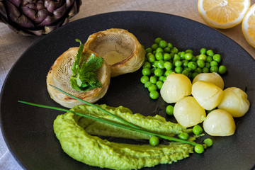 Plate of cooked artichokes, served with peas and potatoes