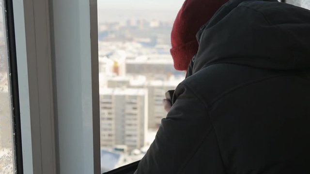 A beardless man with compact camera takes pictures of the winter city from the window from a height