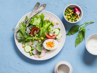 Fresh vegetable salad with tomatoes, radish, green herbs and boiled egg on a light blue stone background. Healthy Breakfast or snack