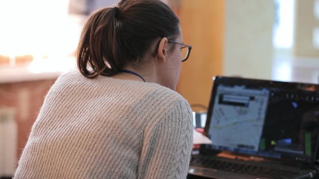 Young woman in glasses and a ponytail hairstyle works behind black laptop