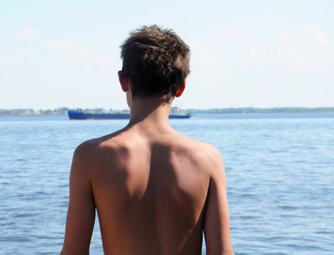 A boy looking at the tanker on the river