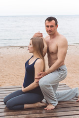 Fototapeta na wymiar Man and pregnant woman are doing yoga on the beach