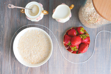 Healthy breakfast: oatmeal in the glass jar, oatmeal pooridge in the white plate, milk, sugar and a few strawberries
