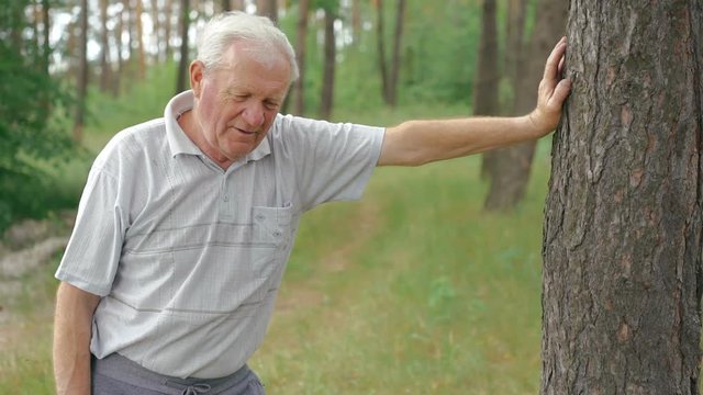Old man resting near the tree after exercises, breathing