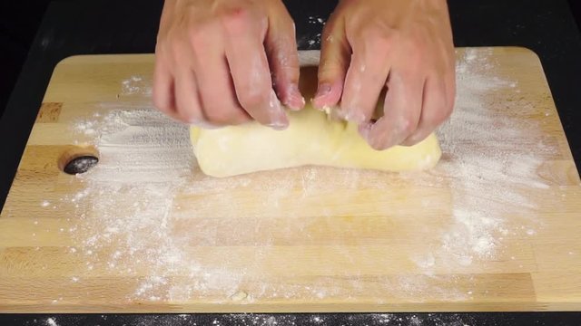 Man hands kneadding dough on light wooden cutting board