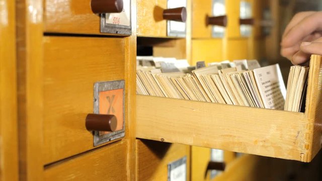 Man looking for a book in the library card catalog