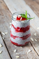 Raw vegan dessert: Chia seeds pudding with strawberries, mint and almond petals on a wooden background