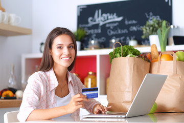 Smiling woman online shopping using tablet and credit card in kitchen