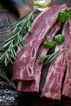 Closeup of raw beef ribs with rosemary, green basil and sea salt