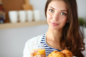 Young woman with glass of juice and cakes standing in kitchen .