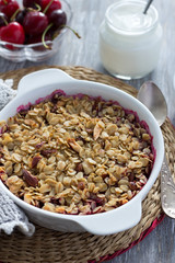 Homemade cherry crumble with oatmeal and almonds with fresh cherry and yogurt on a light wooden table