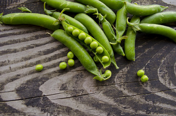 Vintage wooden surface for design with beautifully pods of green peas. Young fresh green peas on old wooden background.