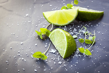 Fototapeta na wymiar Lime Wedges with Sea Salt and Micro Herbs over Slate