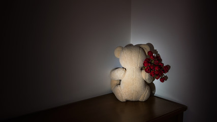 Low key image of Teddy Bear’s concept  holding artificial red rose facing the wall