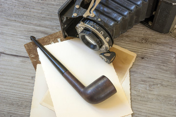 Old retro camera with tobacco pipe on vintage wooden board