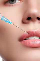 Closeup of beautiful woman gets injection in her lips. Full lips. Beautiful face and the syringe (plastic surgery and cosmetic injection concept).

