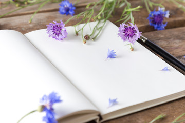 A notebook and cornflowers on a wooden table 