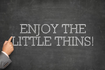 Enjoy the Little Things text on blackboard with businessman hand pointing