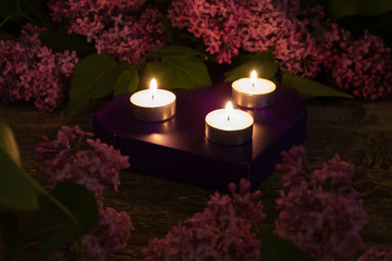 Composition of lilac and burning candles on wooden background closeup. dark toned photo. Shallow depth of field. Focus on the center candle.