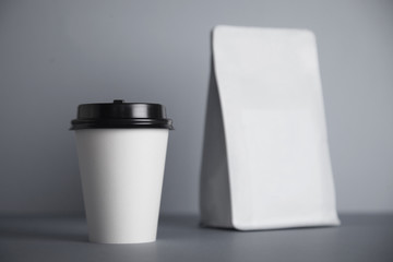 One focused take away white paper cup with black cap presented near blank white bag, isolated on of simple gray background