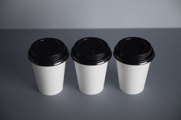 Three focused take away white paper cups with closed black caps, top view, isolated on simple gray background