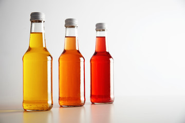 Three glass bottless with colored drinks inside: red, orange, yellow. Presented on white table, isolated on white. Ready for labeling and sale