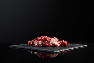 Pieces of raw fresh meat isolated on black on stone board mirrored