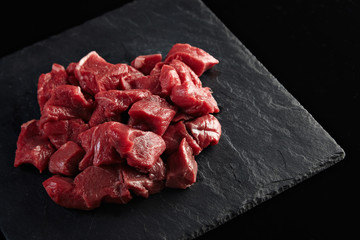 Pieces of raw fresh meat isolated on black stone board on side of the image