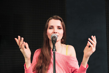 Young singing woman inro the microphone close-up. Beautiful woman in pink dress sings into the micriphone, hands are rised up. Songing woman looking at camera