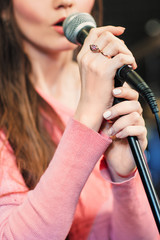 Closeup of singing caucasian woman. Young unrecognizable woman emotionally sings into the microphone, holding it with two hands.